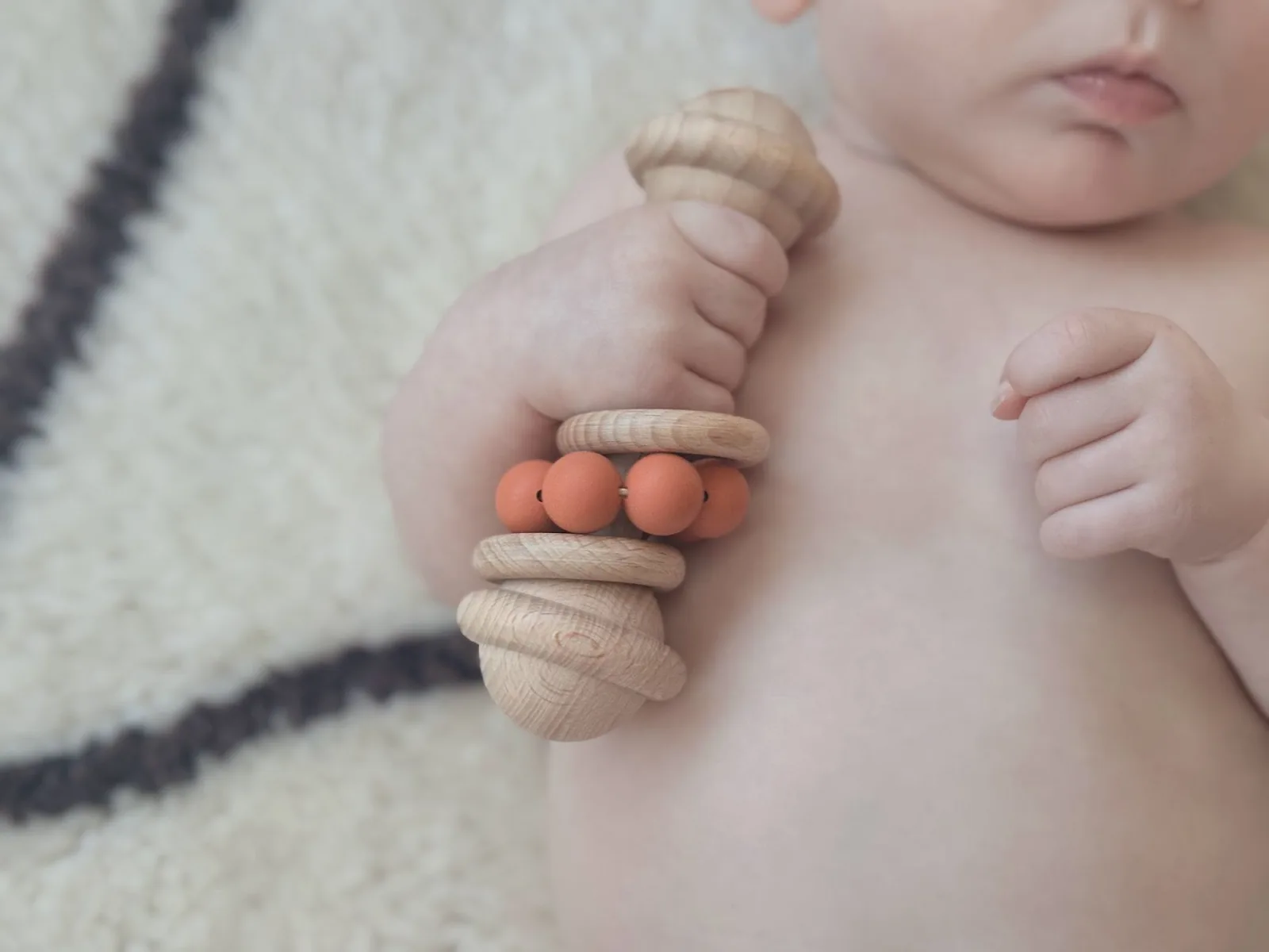 Baby holding a wooden and orange silicone bead rattle from a BurbleBox
